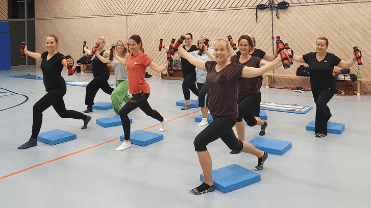 Gruppe von Frauen in Sportkleidung, die mit Hanteln auf blauen Step-Brettern &Uuml;bungen durchf&uuml;hren.