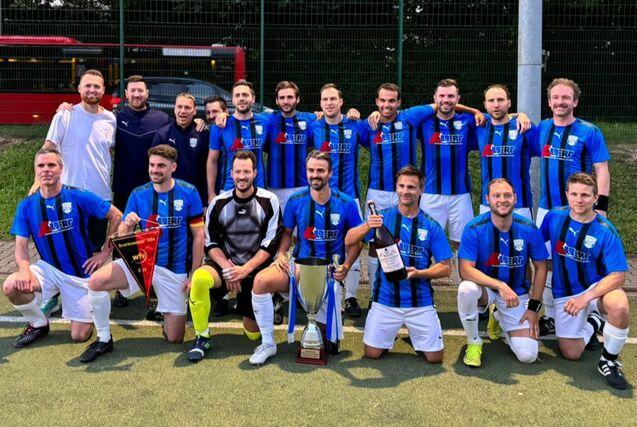 Mannschaftsfoto einer Fußballmannschaft in blauen Trikots, die Trophäen und Medaillen präsentieren.