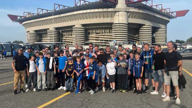Gruppe von Erwachsenen und Kindern posiert vor dem Stadion San Siro unter blauem Himmel.