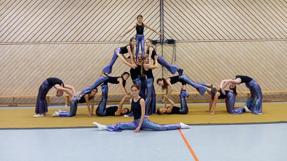 Gruppe von Akrobatinnen formt eine menschliche Pyramide auf einer Sportmatte in einer Turnhalle.