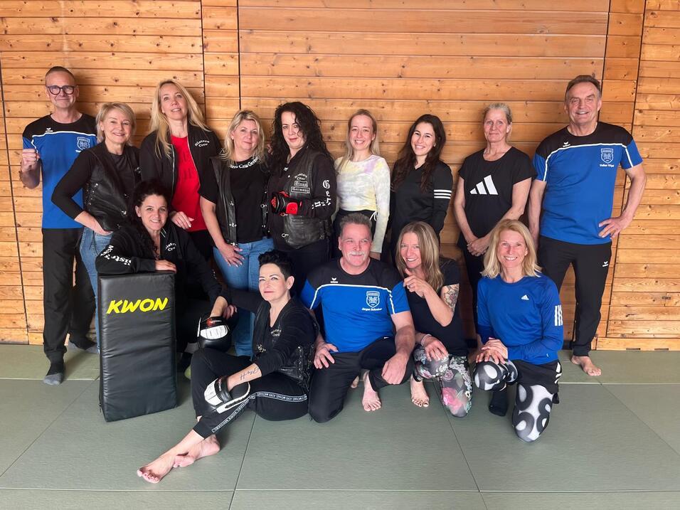 ein Gruppenbild mit Frauen und M&auml;nnern in Sportkleidung, die bei einem Gewaltpr&auml;ventionskurs teilnehmen