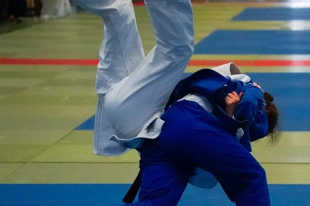 Zwei Judoka in voller Bewegung, einer mit weißem und der andere mit blauem Judogi, auf einer blauen Matte.
