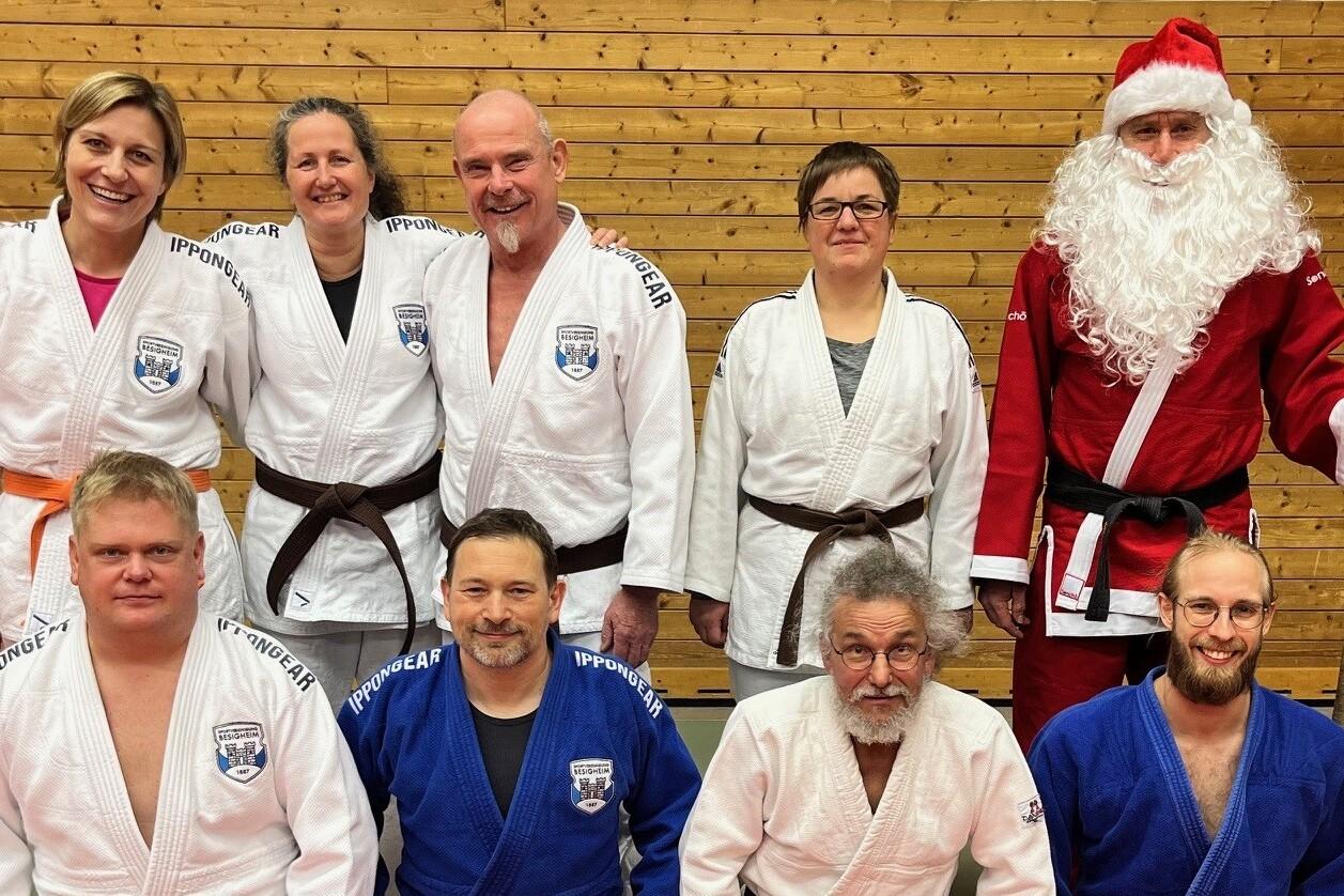Gruppenfoto von acht Judokas in verschiedenen Kimonos, darunter ein Weihnachtsmann, vor einer Holzpaneelwand.