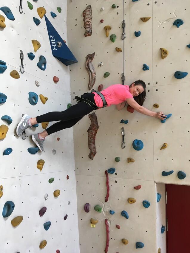 Kletternde Person in pinkem Shirt greift Haltegriff an einer bunten Kletterwand in einer Kletterhalle.