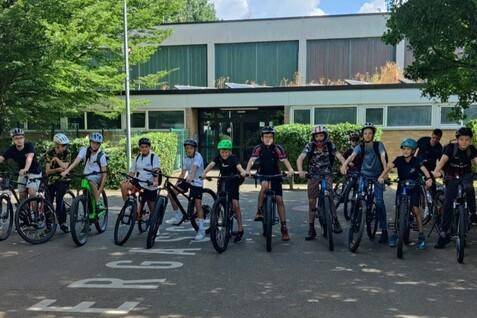 Gruppe von Kindern und Jugendlichen auf Fahrrädern vor einem Gebäude, alle tragen Helme und sind bereit zum Losfahren.