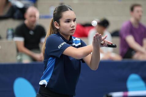 Ein Mädchen in blauem Tischtennis-Shirt hält ein Schläger in einer Hand und balanciert einen Ball in der anderen.