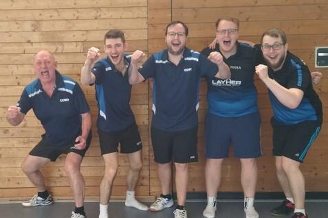 Fünf jubelnde Tischtennisspieler stehen vor einer Holzwand in Sportkleidung und zeigen Siegerpose.