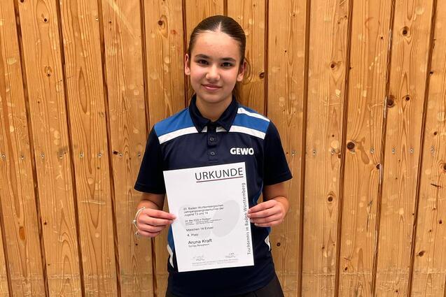 Mädchen in Sportkleidung hält eine Urkunde vor einer Holzvertäfelung in einer Sporthalle.