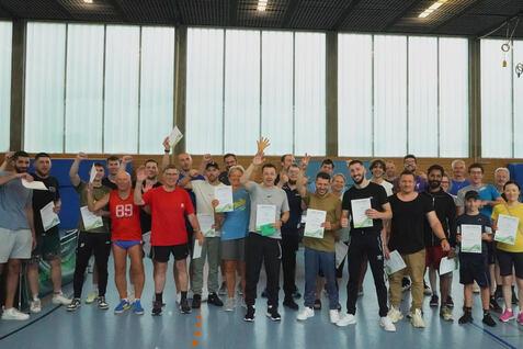 Gruppenzusammenkunft mit Teilnehmern, die Urkunden in einer Sporthalle halten und lächeln.