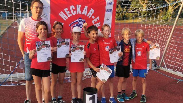 Gruppenfoto von Kindern in roten T-Shirts, die Urkunden halten, vor einem Tor und einer Flagge im Hintergrund.