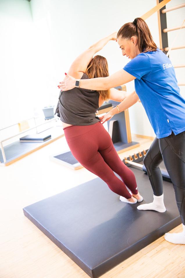 Trainerin unterstützt Frau bei einer Dehnübung auf einer Matte in einem modernen Fitnessraum.