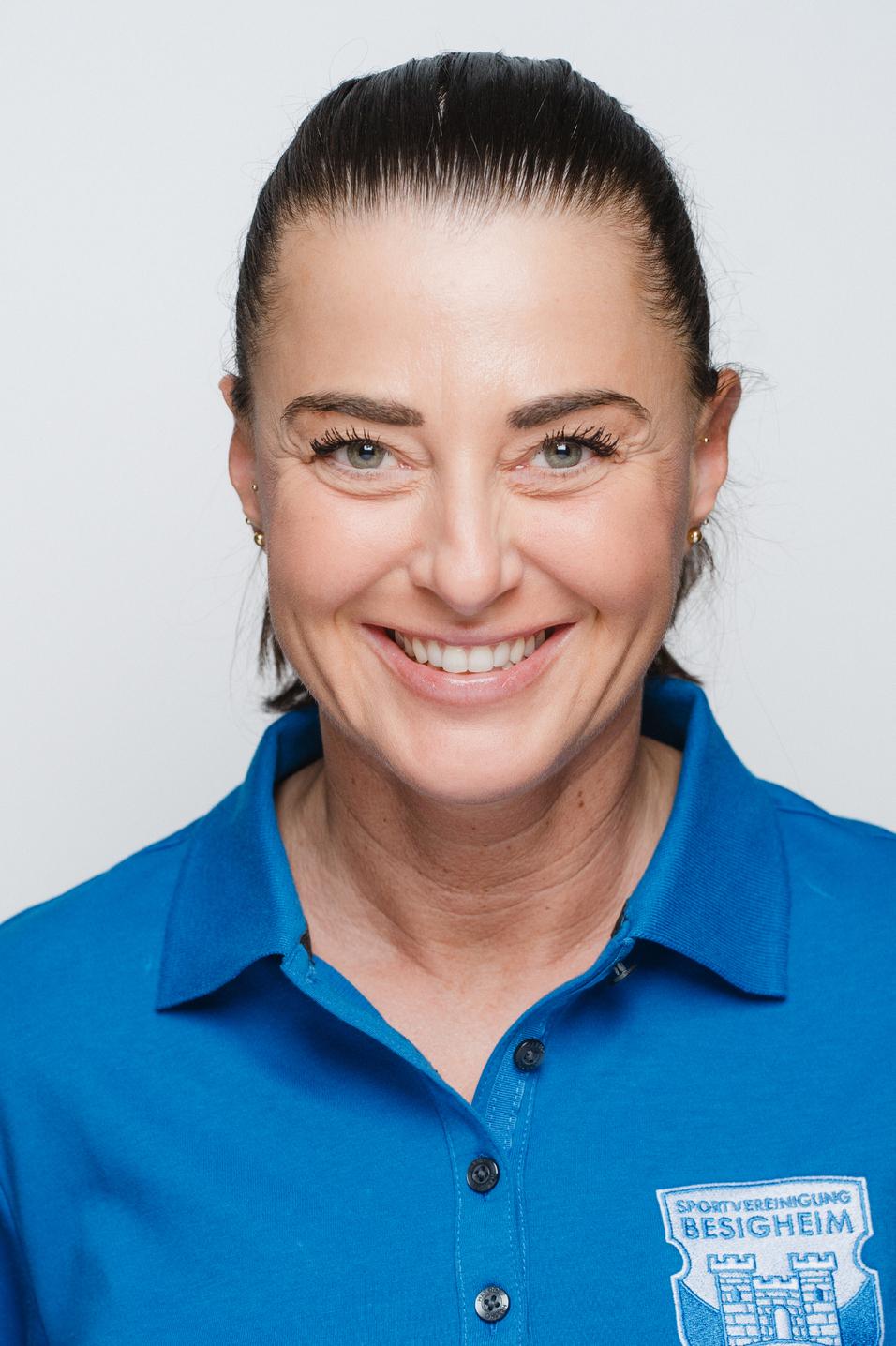 Porträt einer lächelnden Frau in blauer Sportbekleidung, Hintergrund weiß. Sie hat glatte, dunkelharte Haare.