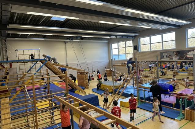verschiedene Ger&auml;te in der Sporthalle sind aufgebaut. Kinder toben darauf