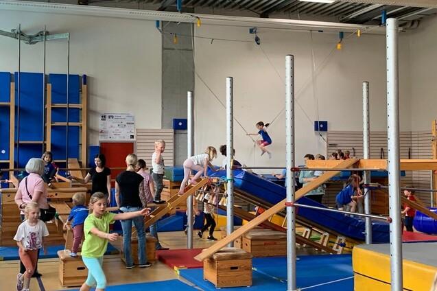 Kindern beim Spielen in einem Turnraum mit Klettergerüst, Rutschen und verschiedenen Turngeräten.