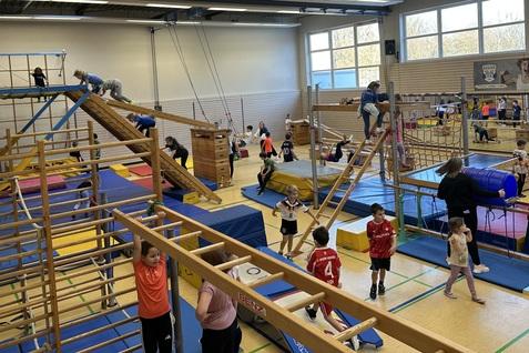 verschiedene Ger&auml;te in der Sporthalle sind aufgebaut. Kinder toben darauf