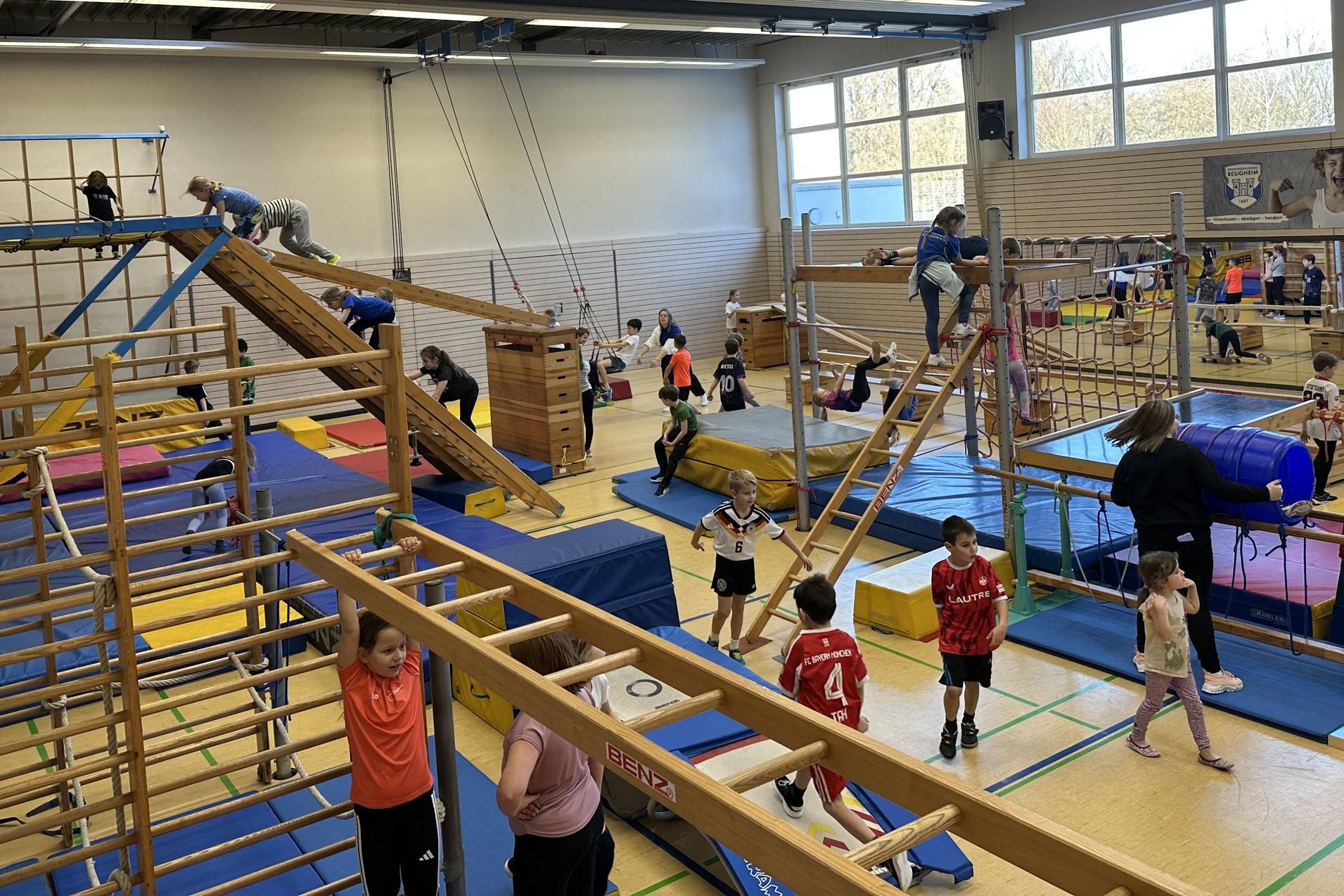 verschiedene Geräte in der Sporthalle sind aufgebaut. Kinder toben darauf