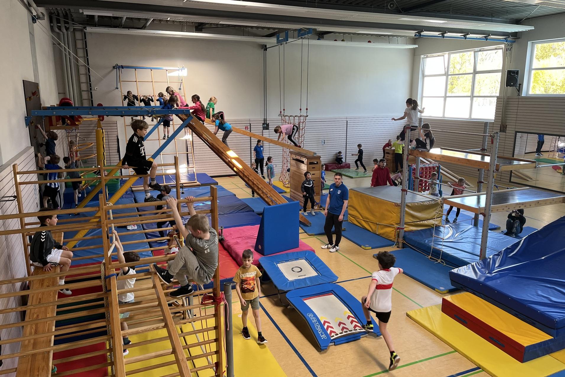 verschiedene Ger&auml;te in der Sporthalle sind aufgebaut. Kinder toben darauf