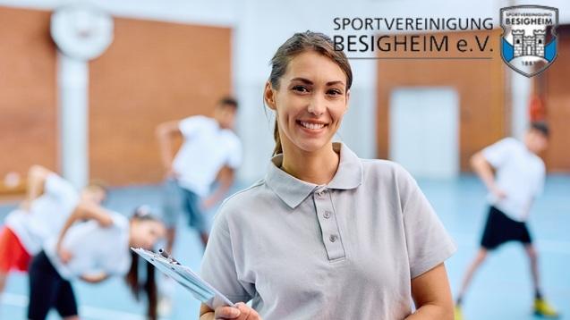 Lächelnde Frau mit Clipboard steht im Vordergrund, während im Hintergrund eine Gruppe in einer Sporthalle Übungen macht.