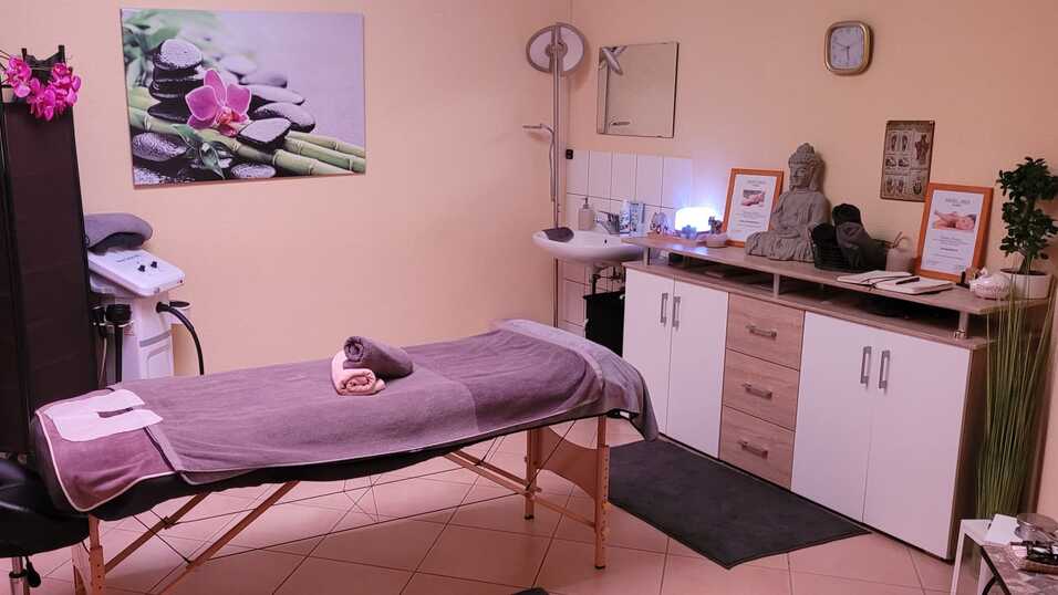 Entspannungsraum mit Massagetisch, Handt&uuml;chern, Pflanzen und dekorativen Elementen an W&auml;nden und M&ouml;beln.