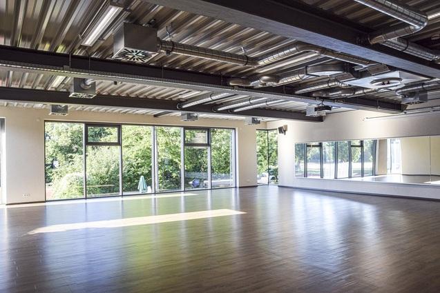 Heller, moderner Raum mit Holzfußboden und großen Fenstern, die Ausblick auf grüne Bäume bieten.