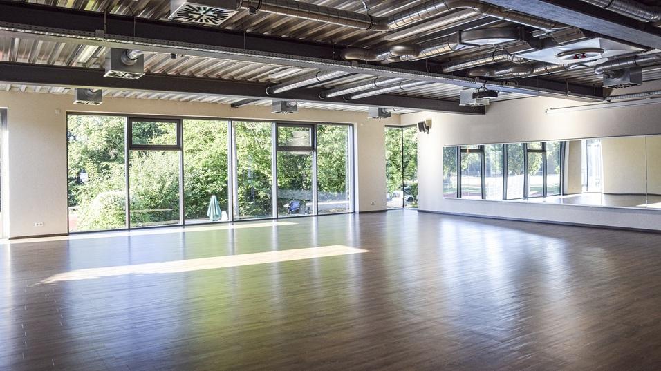 Heller, moderner Raum mit Holzfu&szlig;boden und gro&szlig;en Fenstern, die Ausblick auf gr&uuml;ne B&auml;ume bieten.