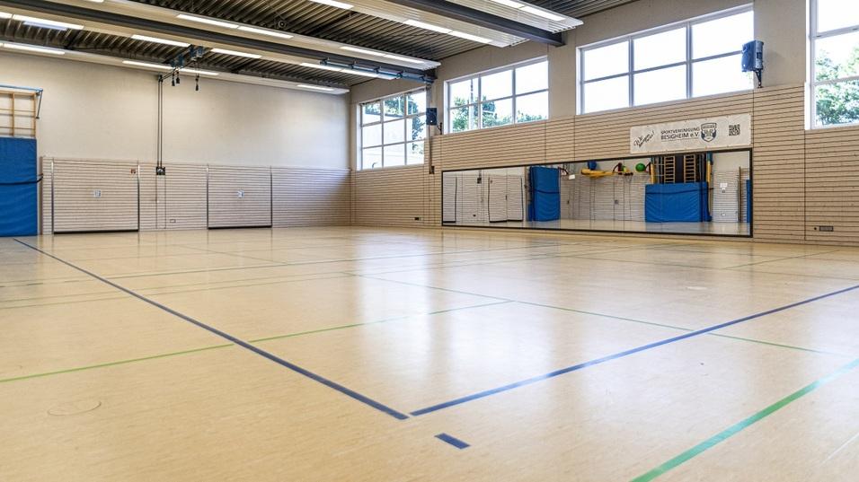 Leere Sporthalle mit Holzfußboden, Fenstern, Wandspiegeln und blauen Matten an der Seite.