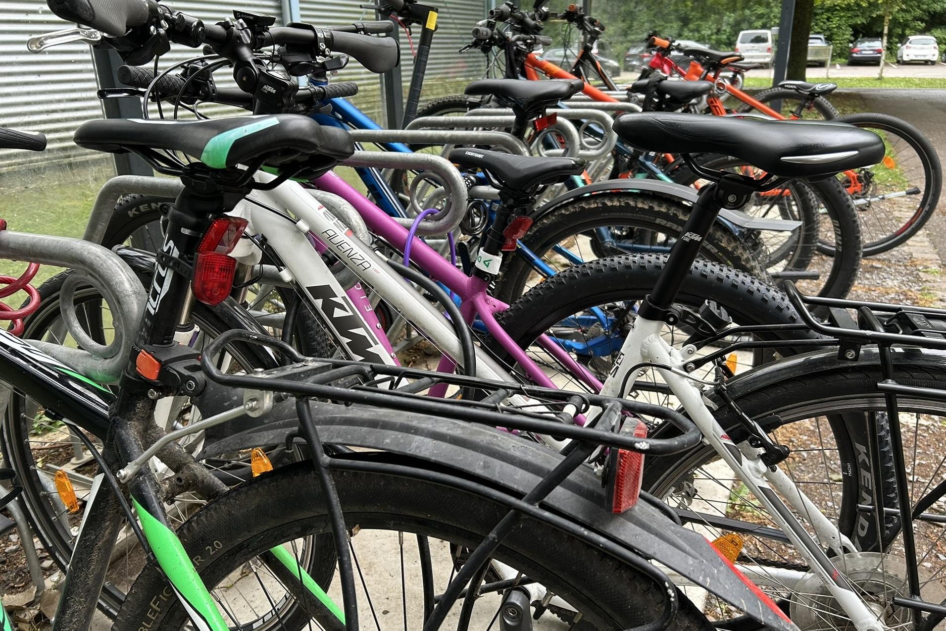 Bunte Fahrräder stehen in einem Fahrradständer, mit Fokus auf Details wie Sattel, Lenker und Räder.