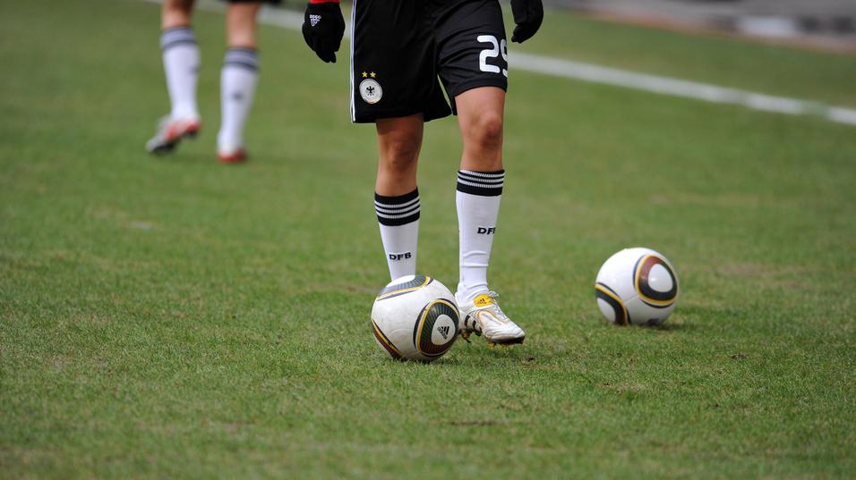 Nahaufnahme eines Fußballspielers mit einem Ball auf dem Rasen, im Hintergrund ein weiterer Ball.
