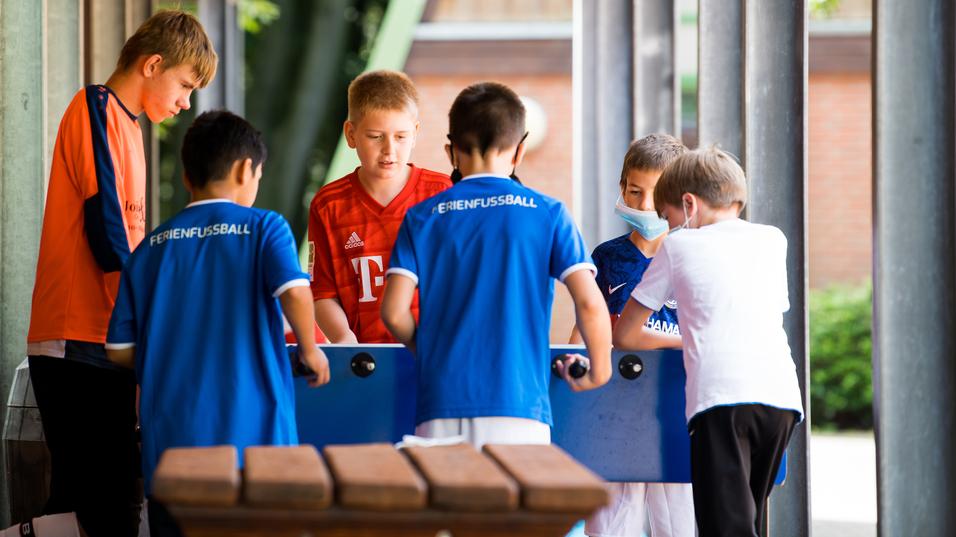 Sechs Kinder spielen gemeinsam mit einem Tischkicker unter einem überdachten Bereich.