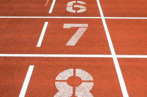 Nahaufnahme einer roten Laufbahn mit den Startnummern 1 bis 8 und grünem Rasen im Hintergrund.