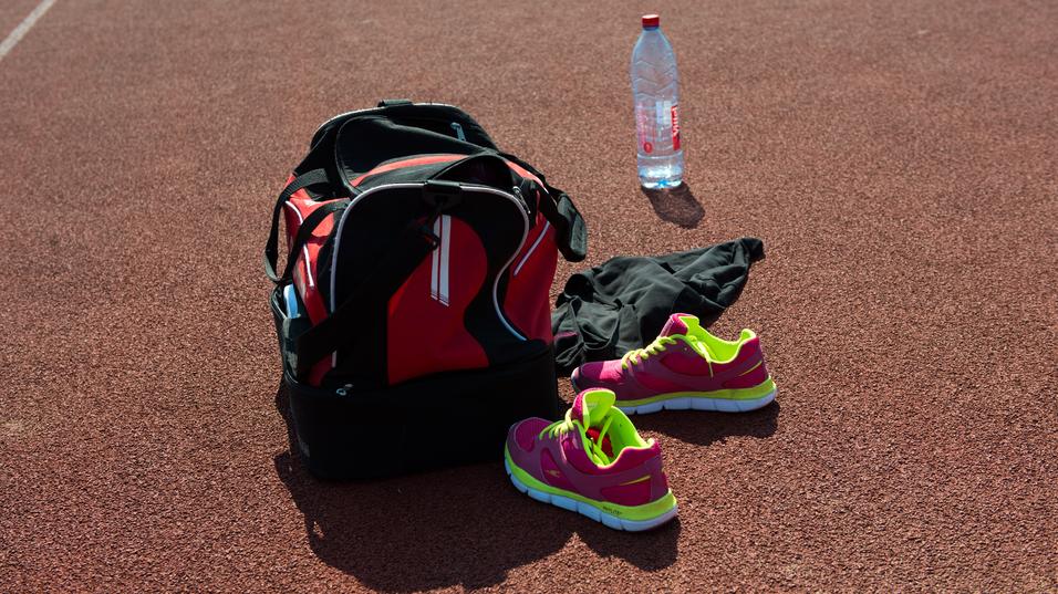 Sporttasche, pinke Sportschuhe, schwarze Kleidung und eine Wasserflasche auf einer orangefarbenen Laufbahn.