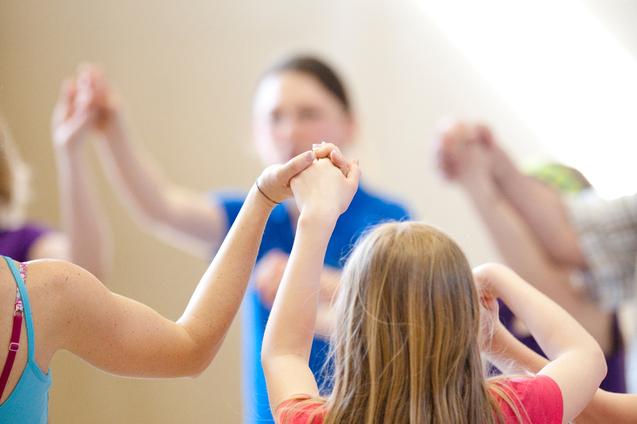 Gruppe von Kindern hält sich in einem gemeinsamen Kreis an den Händen, während sie in einer Sporthalle aktiv sind.