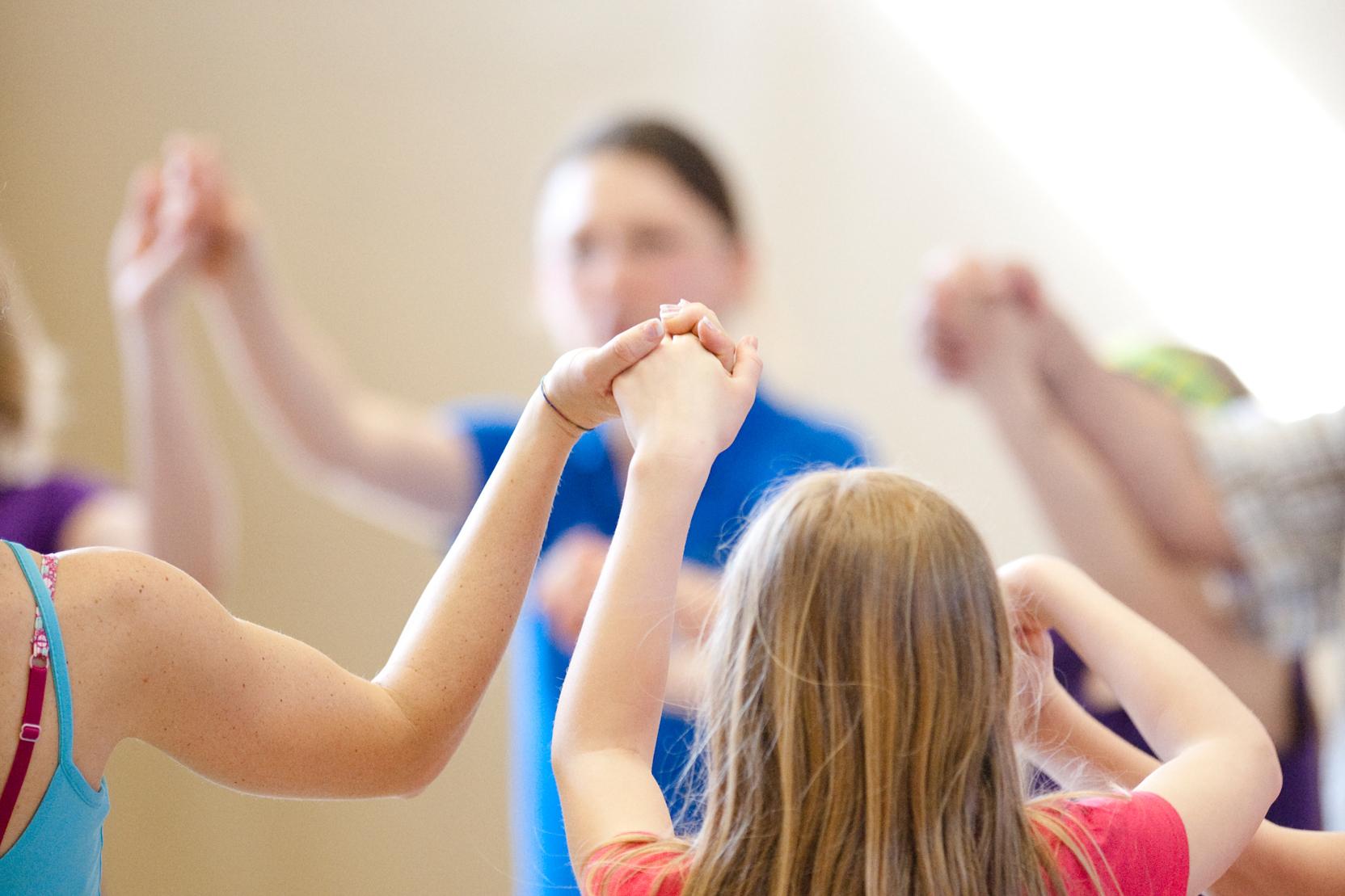 Gruppe von Kindern hält sich in einem gemeinsamen Kreis an den Händen, während sie in einer Sporthalle aktiv sind.